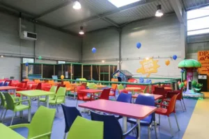 L'image montre une salle de Gulli Parc avec des tables et des chaises colorées, ainsi que des jeux au fond de la salle.